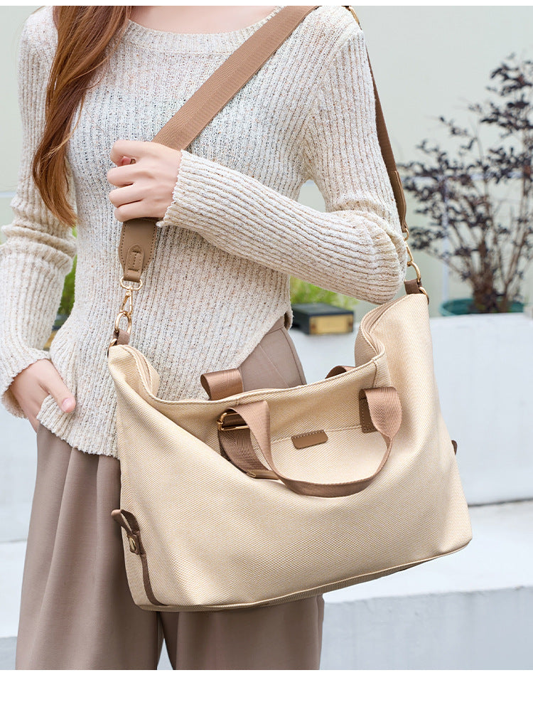 Structured woven duffel bag with dual tan webbing handles, detachable shoulder strap, top zip closure, and gold-tone