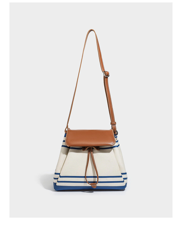 Cream canvas bucket bag with blue horizontal stripes, tan leather-look flap and trim, drawstring closure, silver-tone, detail