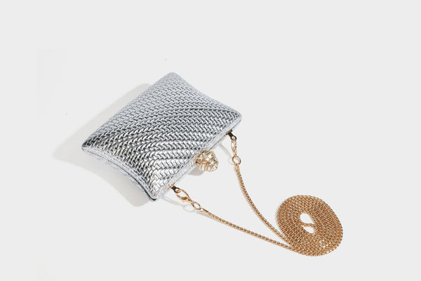 Small structured rectangular metallic woven-texture clutch bag with jeweled knob clasp and gold-tone chain strap, detail view