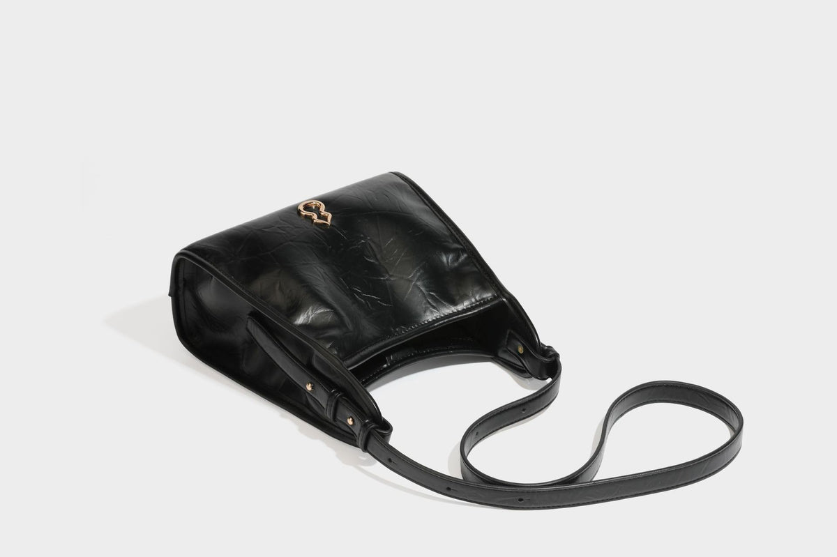 Strukturierte, trapezförmige Schultertasche aus glänzender, geknautscht wirkender Lederoptik mit goldfarbenen Beschlägen auf der Vorderseite und langem, verstellbarem