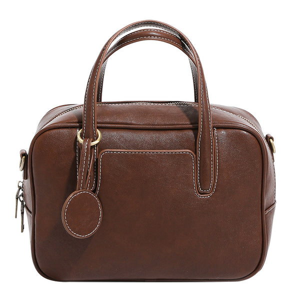 Structured boxy bowling-style tote bag in deep brown leather-look finish with dual top handles, front slip pocket, round