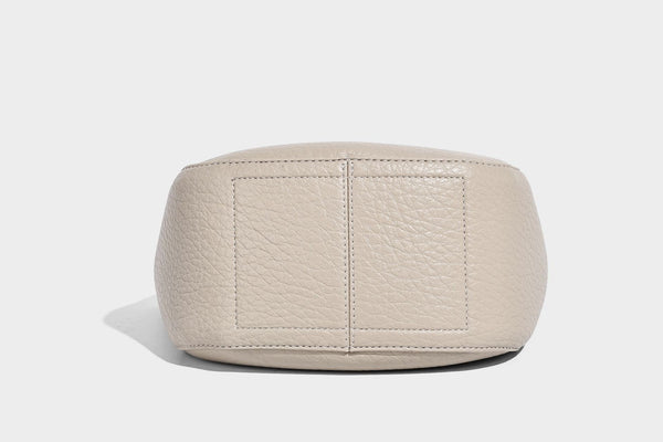 Small pebbled half-moon shoulder bag with dual top handles, detachable crossbody strap, and silver-tone hardware, detail view