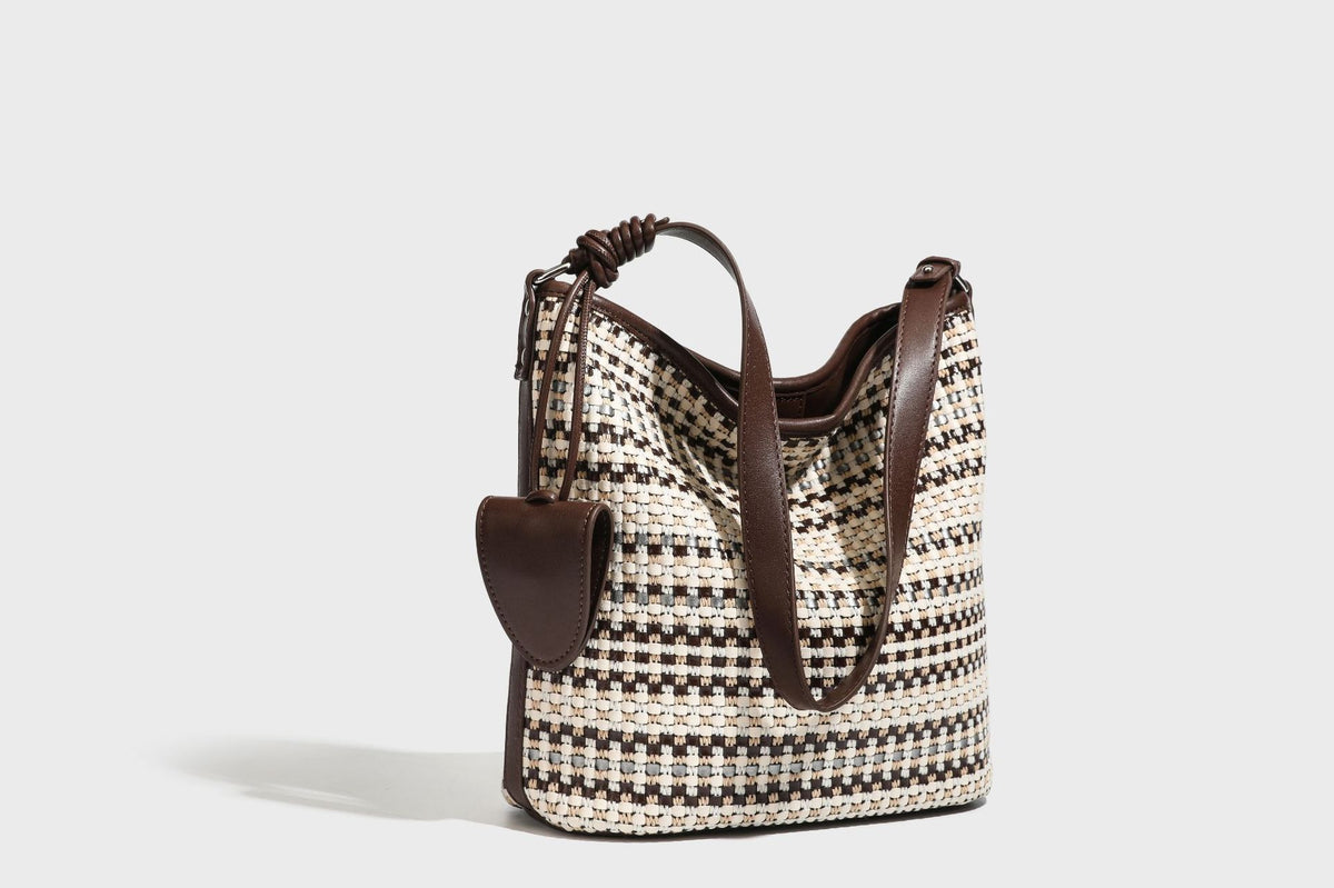 Woven stripe bucket shoulder bag in cream and dark brown with leather-look trim, knotted adjustable strap, and small shield
