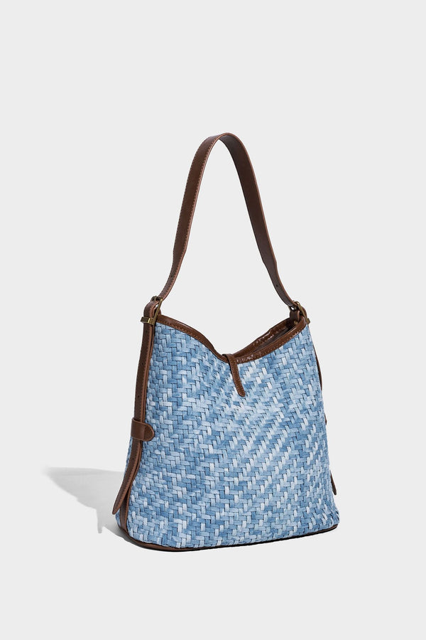 Light blue woven bucket bag with brown leather-look trim, gold-tone hardware, adjustable shoulder strap, and decorative bead