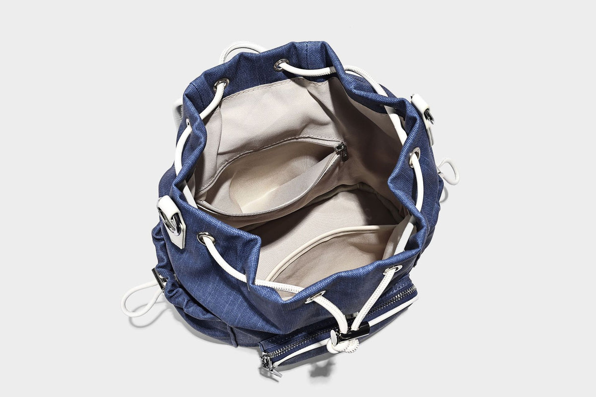 Compact denim drawstring backpack with white leather-look piping, flap-top buckle closure, front zip pocket, and silver-tone