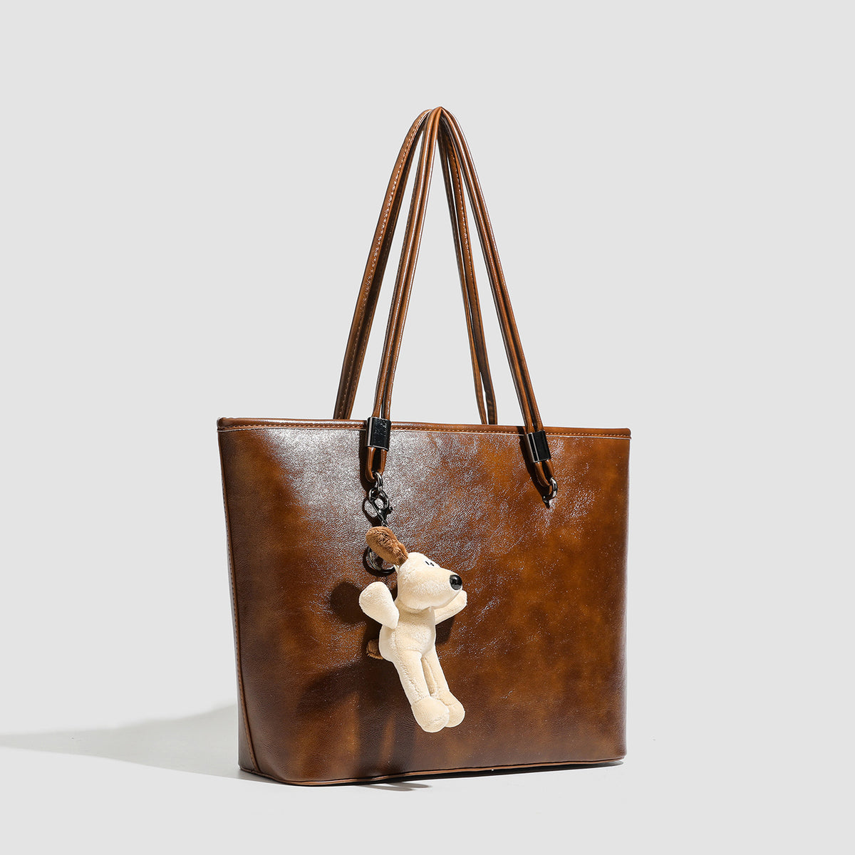 Large structured brown vintage-finish tote bag with double shoulder handles, gunmetal hardware, and plush bear charm, detail