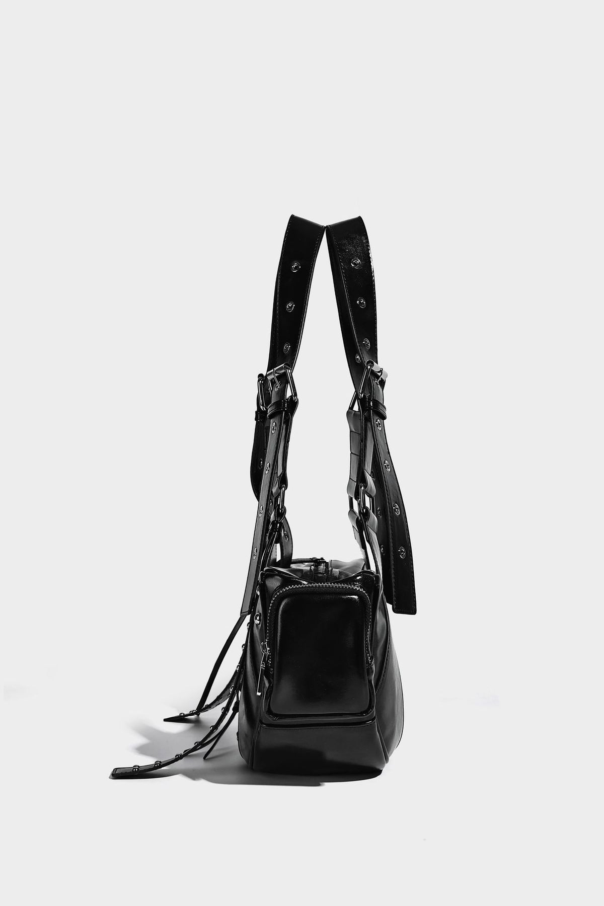 Glossy black crescent shoulder bag with silver-tone rivets, multiple zip pockets, and long adjustable studded straps, detail