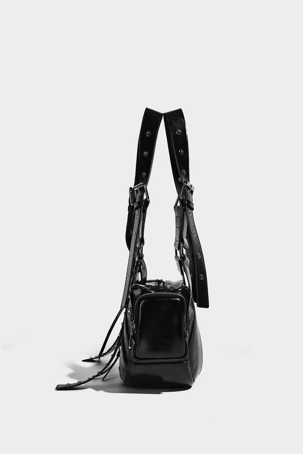 Glossy black crescent shoulder bag with silver-tone rivets, multiple zip pockets, and long adjustable studded straps, detail