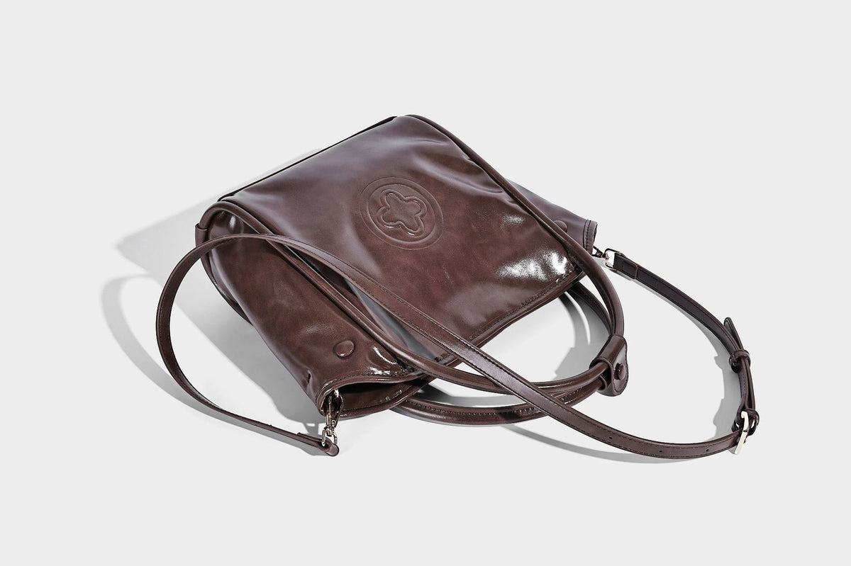 Glossy leather-look structured tote bag with rounded top handles, detachable shoulder strap, embossed front emblem, and side