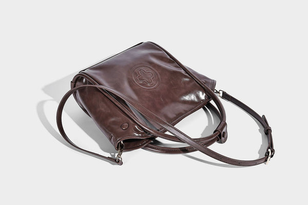 Glossy leather-look structured tote bag with rounded top handles, detachable shoulder strap, embossed front emblem, and side