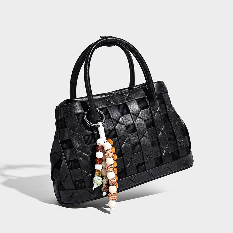 Small structured woven satchel tote with rounded top handles, silver-tone ring hardware, and bead tassel charm, detail view