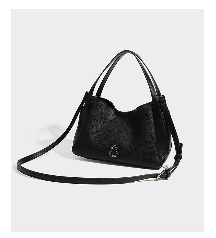 Schwarze Tote-Bag aus genarbtem Material in Lederoptik mit kürbisförmigen Beschlägen in Goldoptik, zwei Henkeln und abnehmbarem Umhängeriemen, Detailansicht