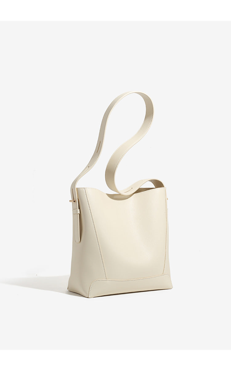 Structured smooth leather-look bucket shoulder bag with long adjustable strap and gold-tone buckle hardware in brown, detail