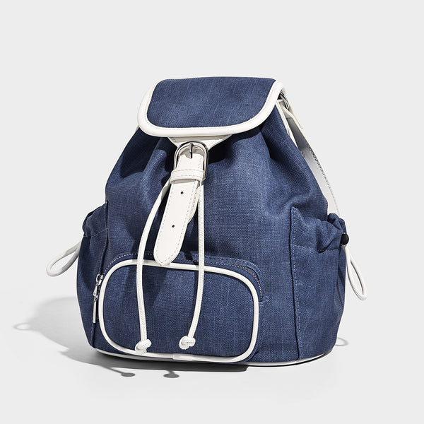 Compact denim drawstring backpack with white leather-look piping, flap-top buckle closure, front zip pocket, and silver-tone