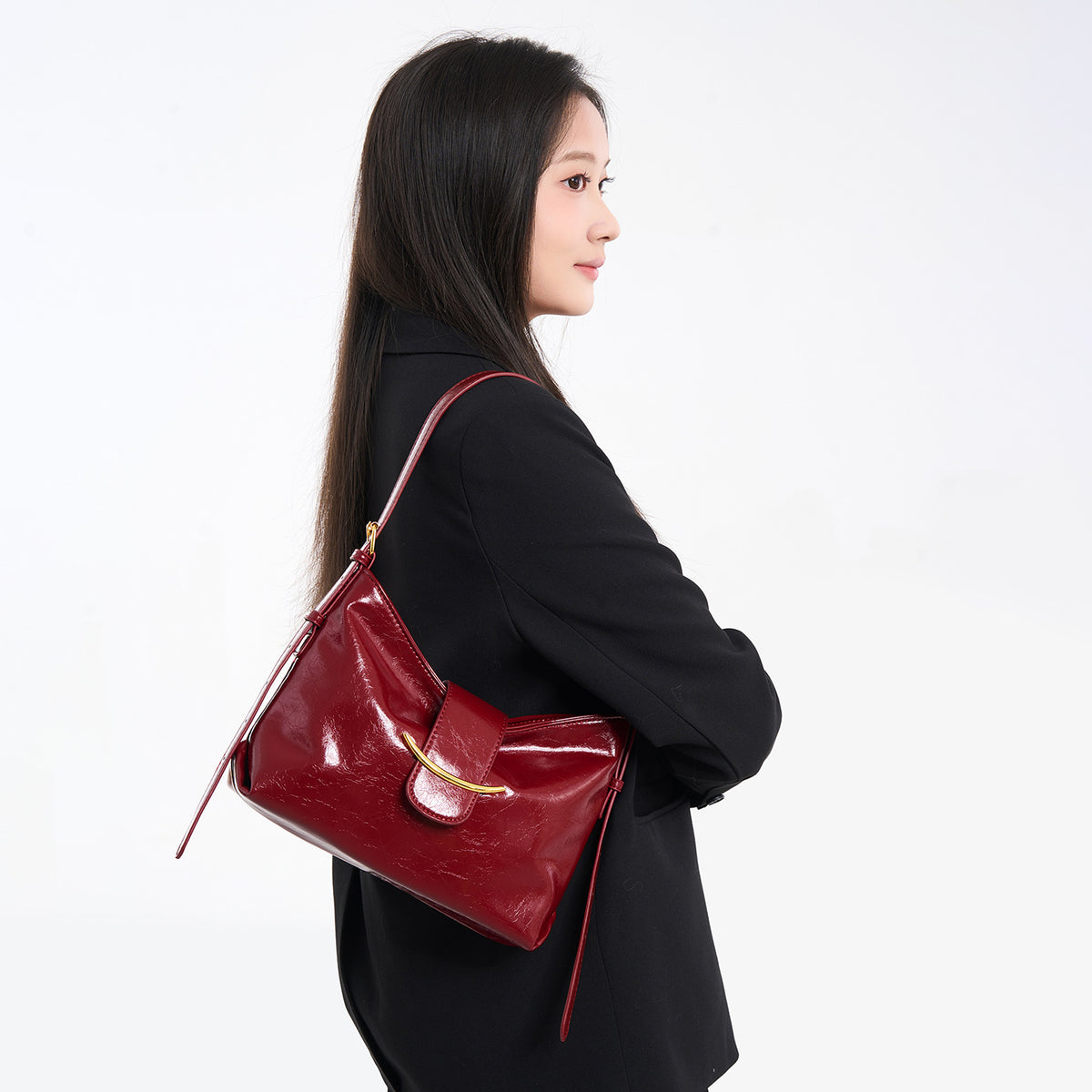 Glossy burgundy leather-look shoulder bag with curved gold-tone bar front closure, crinkled oil-wax texture, and adjustable
