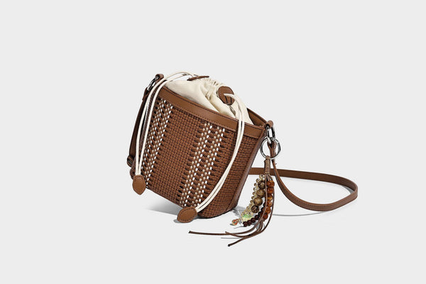 Small woven bucket bag with drawstring top, braided handle, detachable crossbody strap, and silver-tone ring hardware, detail