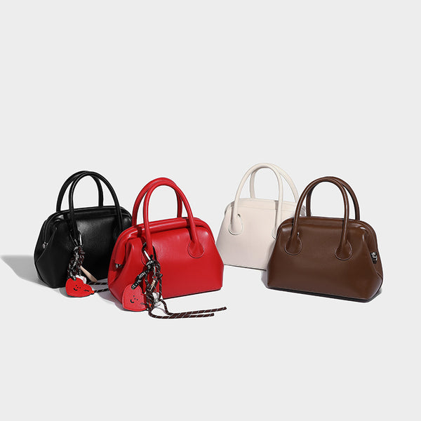 Small structured shell top-handle bag in red with heart charm and braided cord detail, smooth leather-look finish, detail