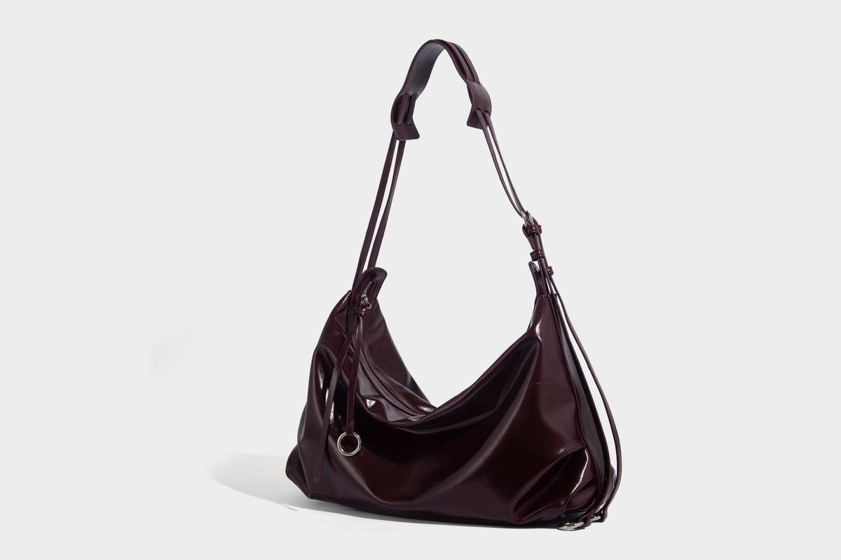 Glossy black slouchy hobo shoulder bag with zip closure, silver-tone ring hardware, and adjustable crossbody strap, detail