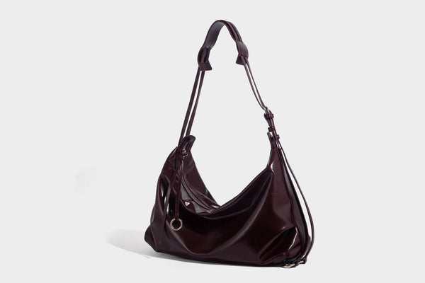 Glossy black slouchy hobo shoulder bag with zip closure, silver-tone ring hardware, and adjustable crossbody strap, detail