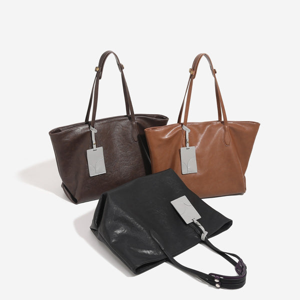 Oversized slouchy leather-look tote bag with long shoulder straps, contrast grey hanging tag, and silver-tone hardware, front