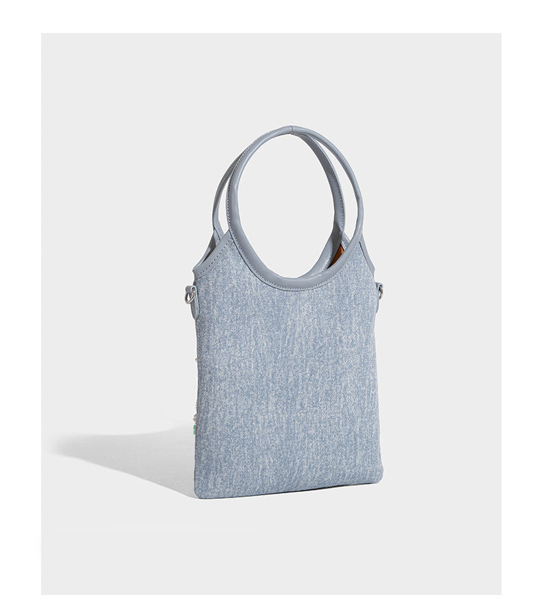 Kleine hellblaue Mini-Tote-Bag aus Stoff mit weißer Perlenblumenverzierung, runden Henkeln, silberfarbenen Beschlägen und