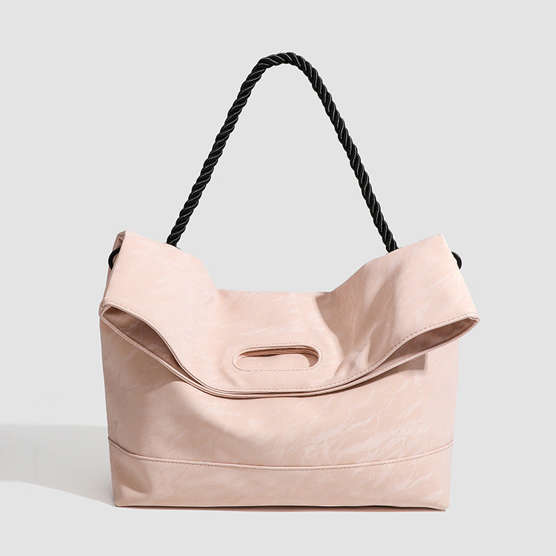 Large blush pink tote bag with twisted black rope handle and oval cutout carry slot, crinkled textured finish, front view