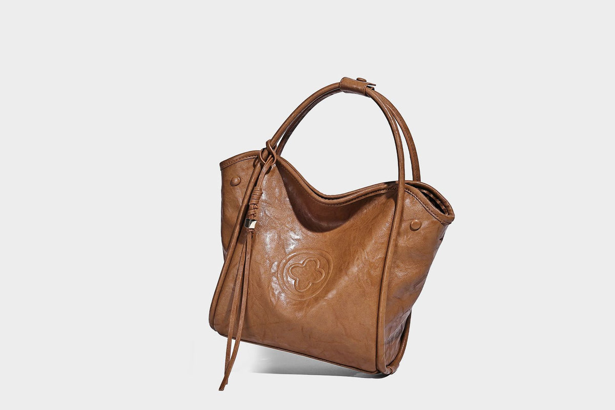Glänzende Tragetasche in geknautschtem Lederlook mit geprägtem kreisförmigem Emblem, Quastenverschluss, zwei Tragegriffen und abnehmbarem