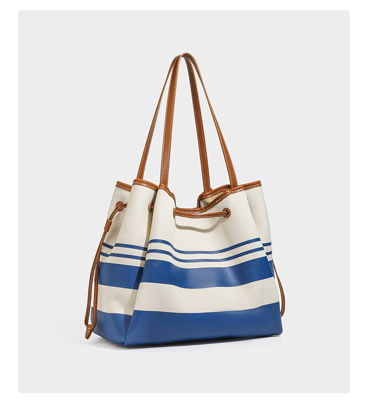 Large cream and navy striped canvas bucket tote bag with tan leather-look trim, drawstring closure, and double shoulder