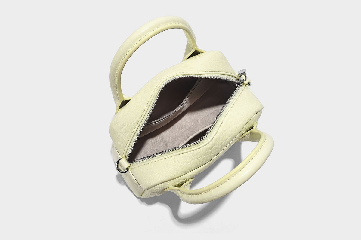 Mini-Tasche mit strukturierter Kuppelform und Tragegriff, in Pastellgelb mit genarbter Lederoptik, silberfarbenen Metallbeschlägen und abnehmbarem