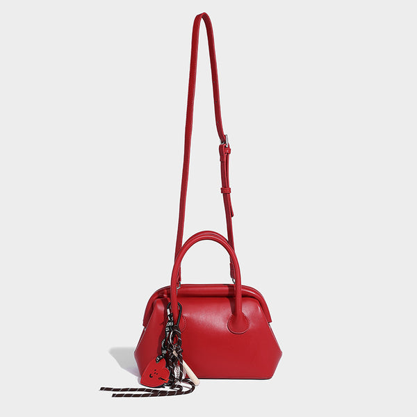 Small structured shell top-handle bag in red with heart charm and braided cord detail, smooth leather-look finish, detail