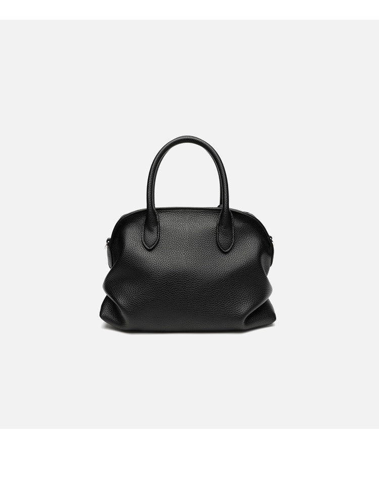 Rounded dome shell handbag in pebbled leather-look finish with twin top handles, zip closure, decorative horse charm, and