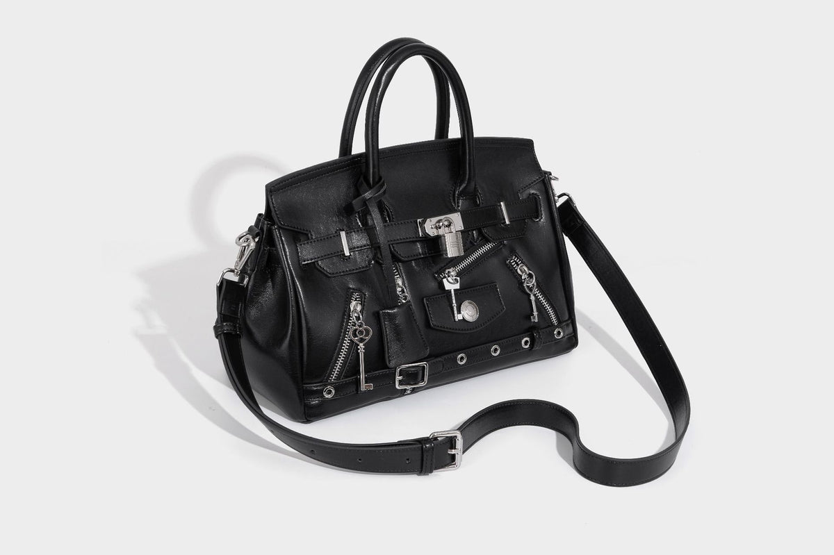 Structured black leather-look satchel bag with silver padlock hardware, front zip pockets, key charms, and top handles