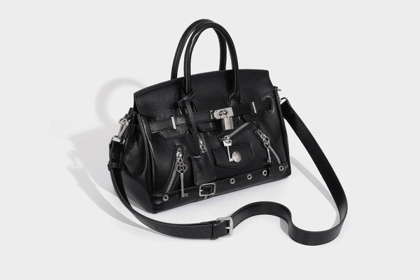 Structured black leather-look satchel bag with silver padlock hardware, front zip pockets, key charms, and top handles