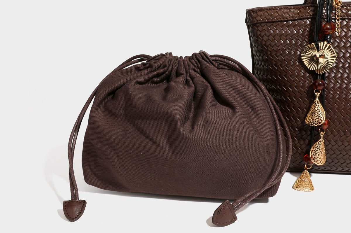 Structured woven leather-look tote bag in dark brown with long shoulder straps, side drawstring ties, and gold filigree
