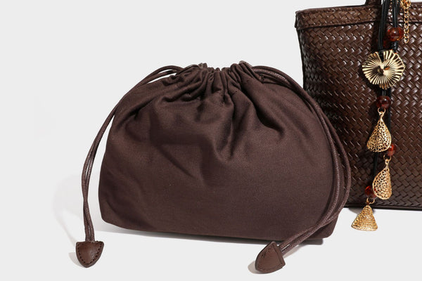 Structured woven leather-look tote bag in dark brown with long shoulder straps, side drawstring ties, and gold filigree