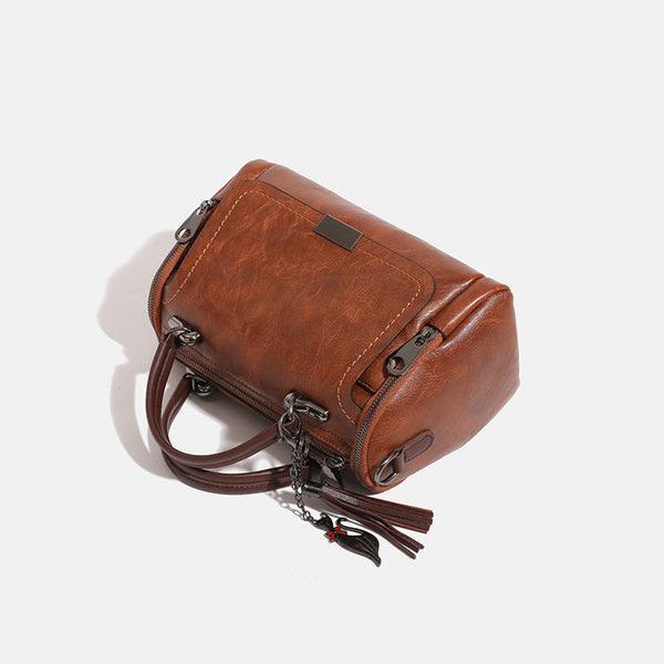 Compact structured barrel bag in distressed leather-look finish with dual top handles, detachable crossbody strap, front zip