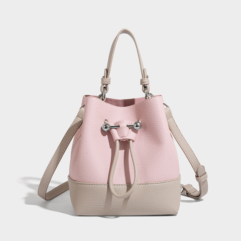 Small two-tone pebbled drawstring bucket bag with tan contrast base, metal toggle hardware, short top handle, and detachable