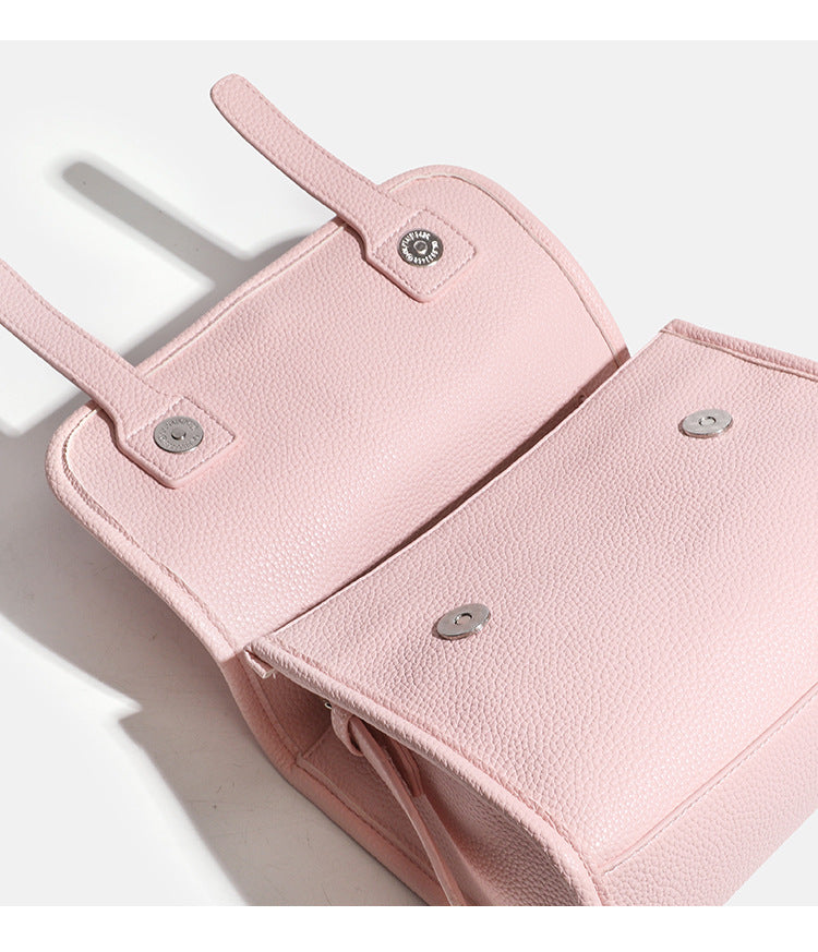 Compact structured flap satchel bag with pebbled texture, snap closure, front strap tabs, and long adjustable crossbody