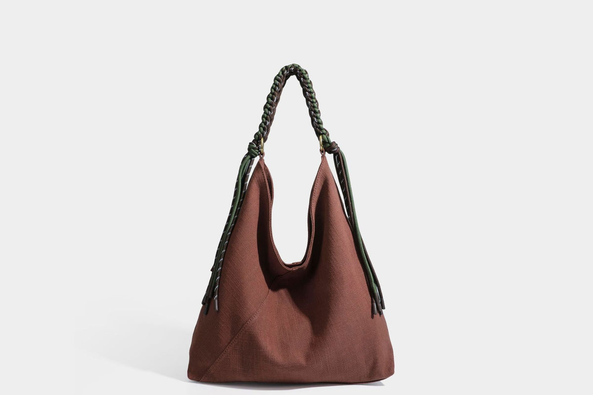 Soft slouchy cream canvas shoulder tote with braided brown and green cord handle, gold-tone ring hardware, and tassel trim