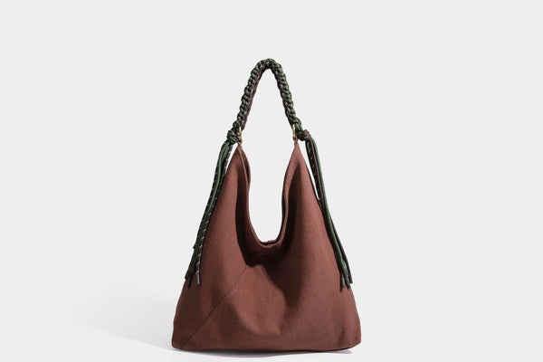 Soft slouchy cream canvas shoulder tote with braided brown and green cord handle, gold-tone ring hardware, and tassel trim