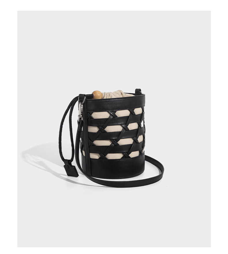 Small cylindrical woven lattice bucket bag with leather-look black trim, beige canvas body, wooden bead drawstring closure