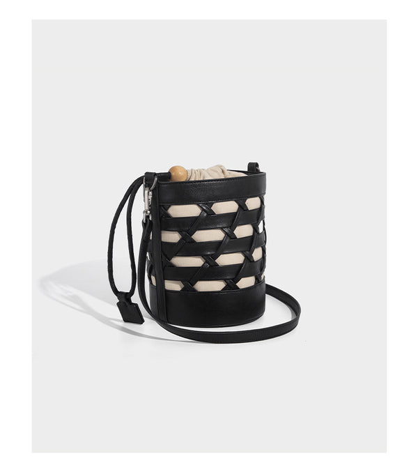 Small cylindrical woven lattice bucket bag with leather-look black trim, beige canvas body, wooden bead drawstring closure