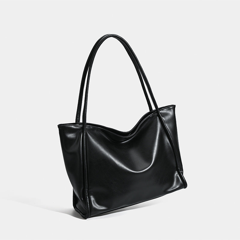Large black glossy leather-look tote bag with dual shoulder straps and gently curved top edge, detail view 2