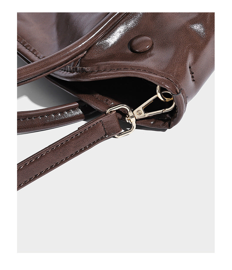 Glossy leather-look structured tote bag with rounded top handles, detachable shoulder strap, embossed front emblem, and side
