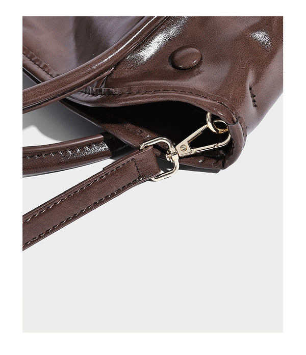 Glossy leather-look structured tote bag with rounded top handles, detachable shoulder strap, embossed front emblem, and side
