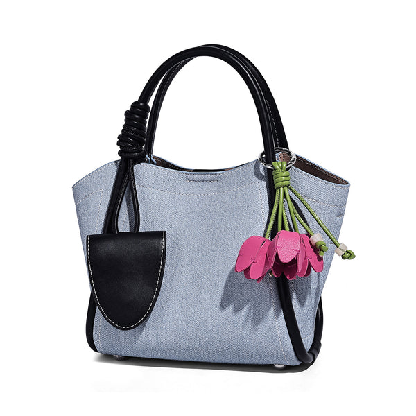 Light blue denim trapezoid tote bag with black leather-look trim, knotted top handles, detachable crossbody strap, front