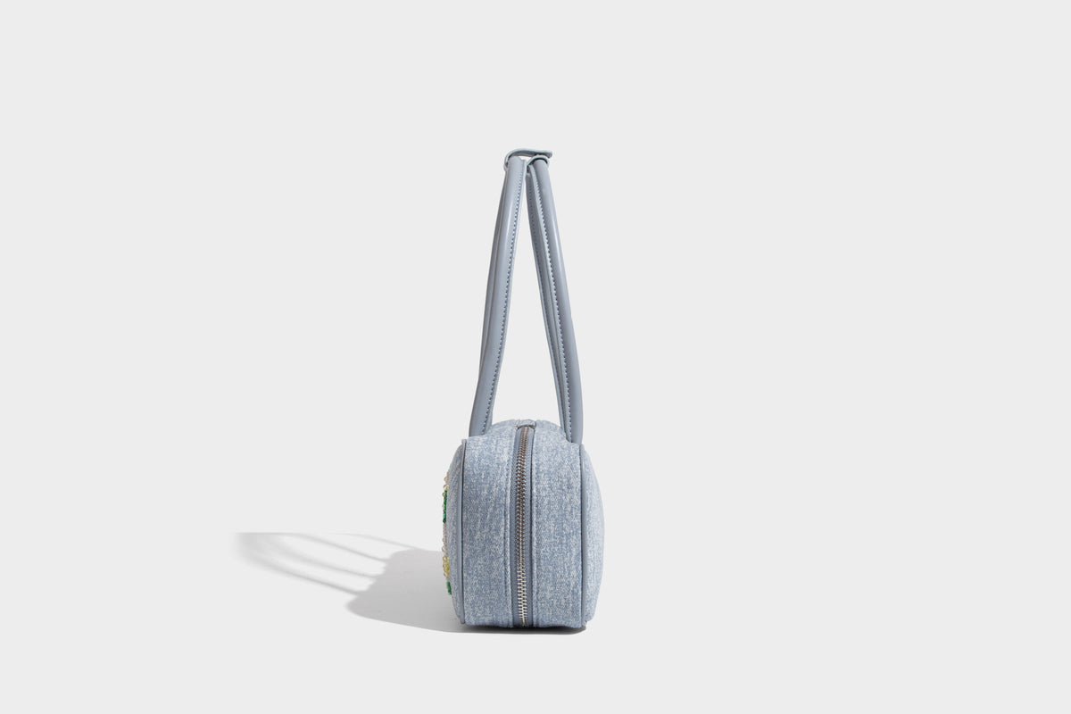 Small structured light blue denim-texture bowling bag with white floral bead embroidery, dual rounded top handles, and