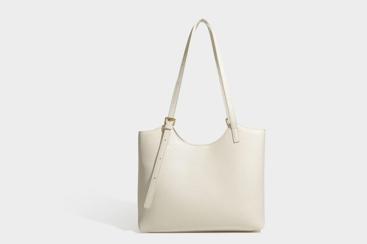 Structured smooth leather-look tote bag with long shoulder strap, gold-tone hardware, and hanging tassel-coin charm, detail