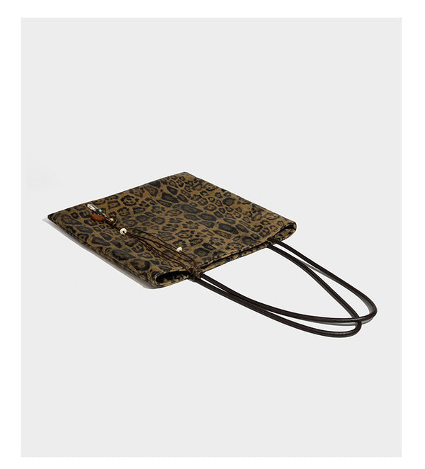 Large leopard print shoulder tote bag in tan and brown with slim dark straps and dangling beaded charm hardware, detail view