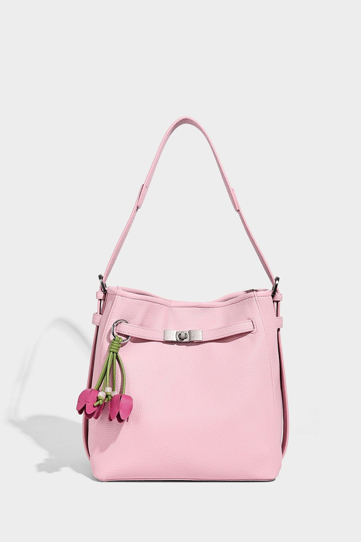 Soft-structured pebbled bucket shoulder bag with front turn-lock strap detail, adjustable strap, and hanging floral tassel